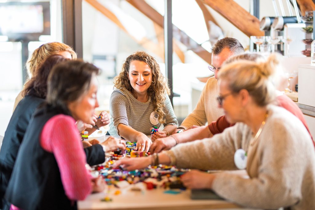 Deelnemers verspreid over meerdere tafels tijdens een evenement met LEGO® bouwstenen